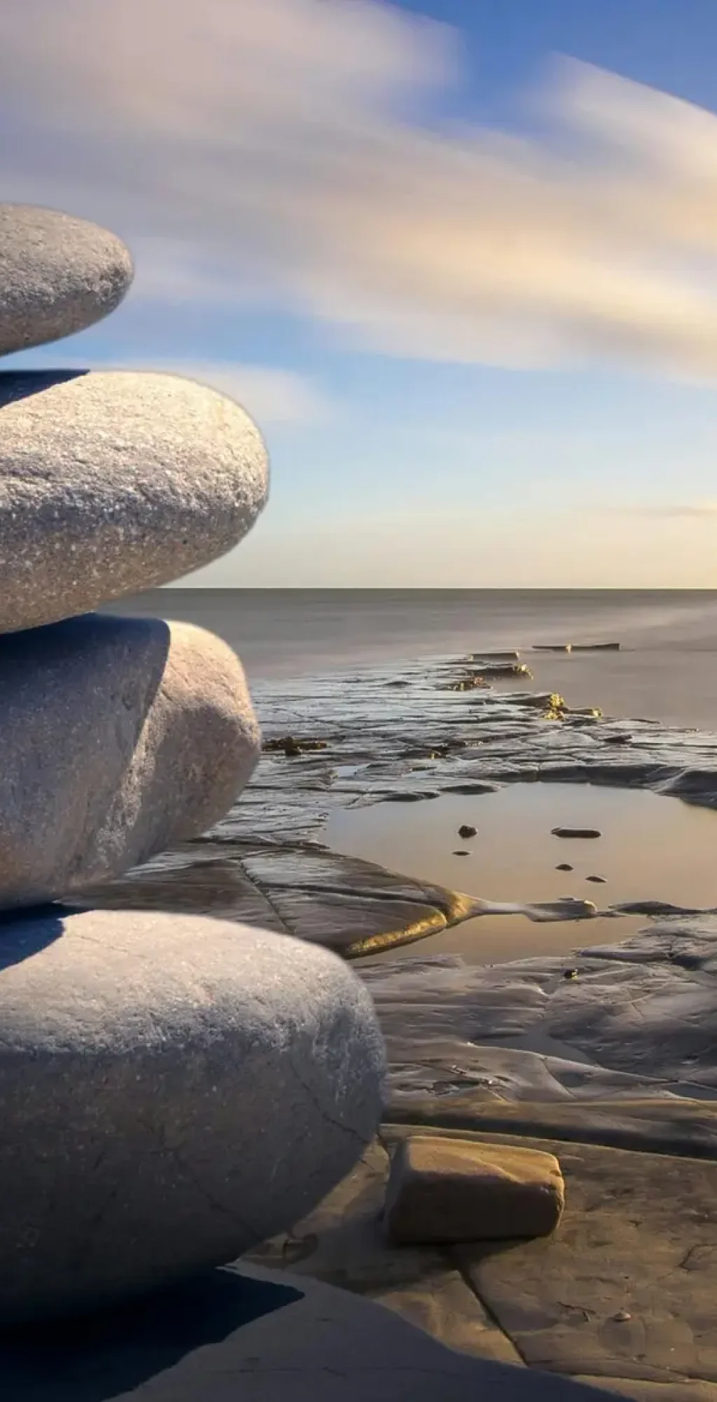 A serene stack of stones on the rocky seashore during a peaceful sunrise, embodying balance and zen.