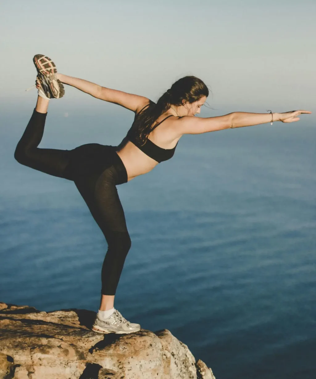 Woman practicing yoga in Dancer's pose on a cliff with ocean view, Cape Town.